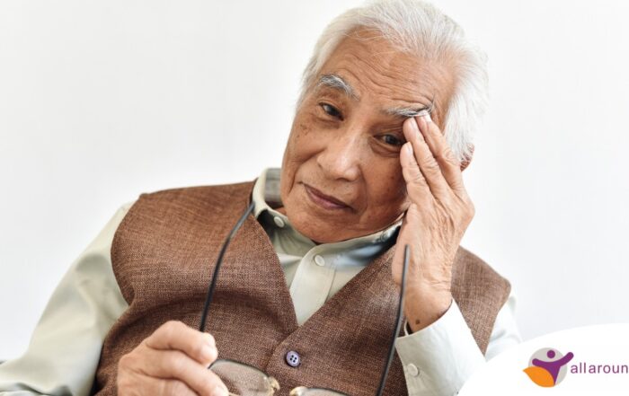 An older adult holds his head and his glasses representing vision problems like macular degeneration.
