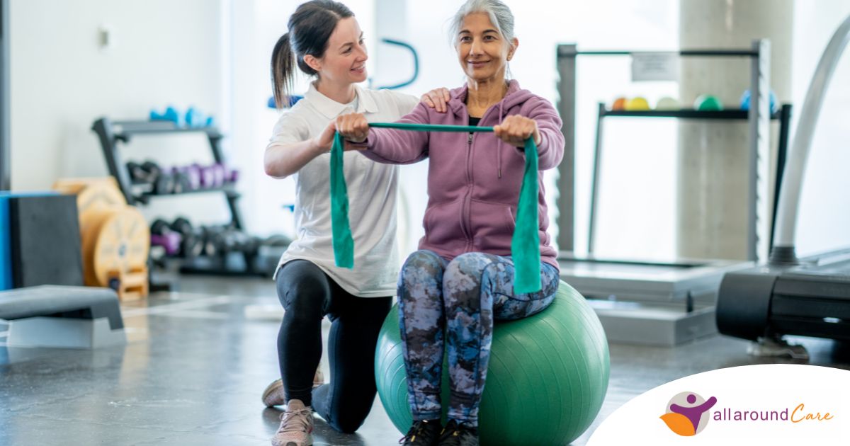 A care provider helps an older woman exercise with a resistance band and an exercise ball, representing how exercise can help with senior fall prevention.